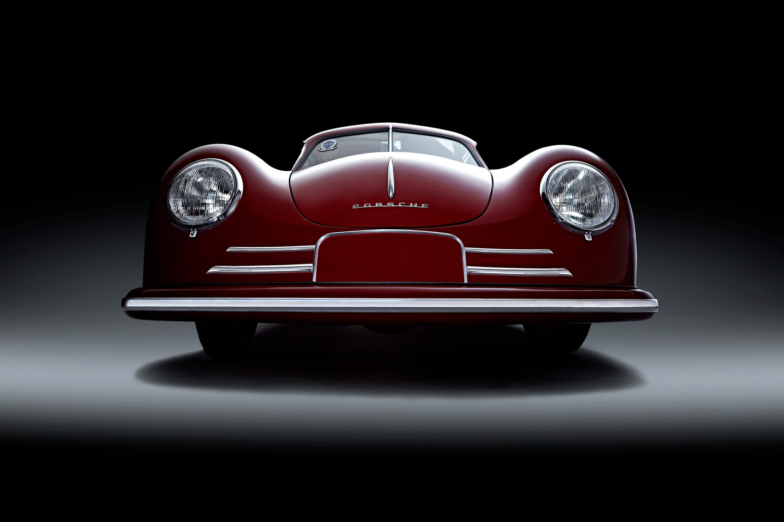 Vorderansicht eines klassischen roten Porsche-Sportwagens, isoliert auf dunklem Hintergrund mit dramatischer Beleuchtung, die seine Kurven und Scheinwerfer hervorhebt.
