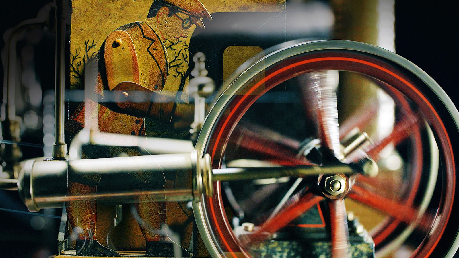 Nahaufnahme eines alten mechanischen Geräts mit einem sich drehenden Schwungrad im Vordergrund und der Illustration eines Mannes mit Hut und Brille im Hintergrund, der teilweise durch Maschinenteile verdeckt ist.