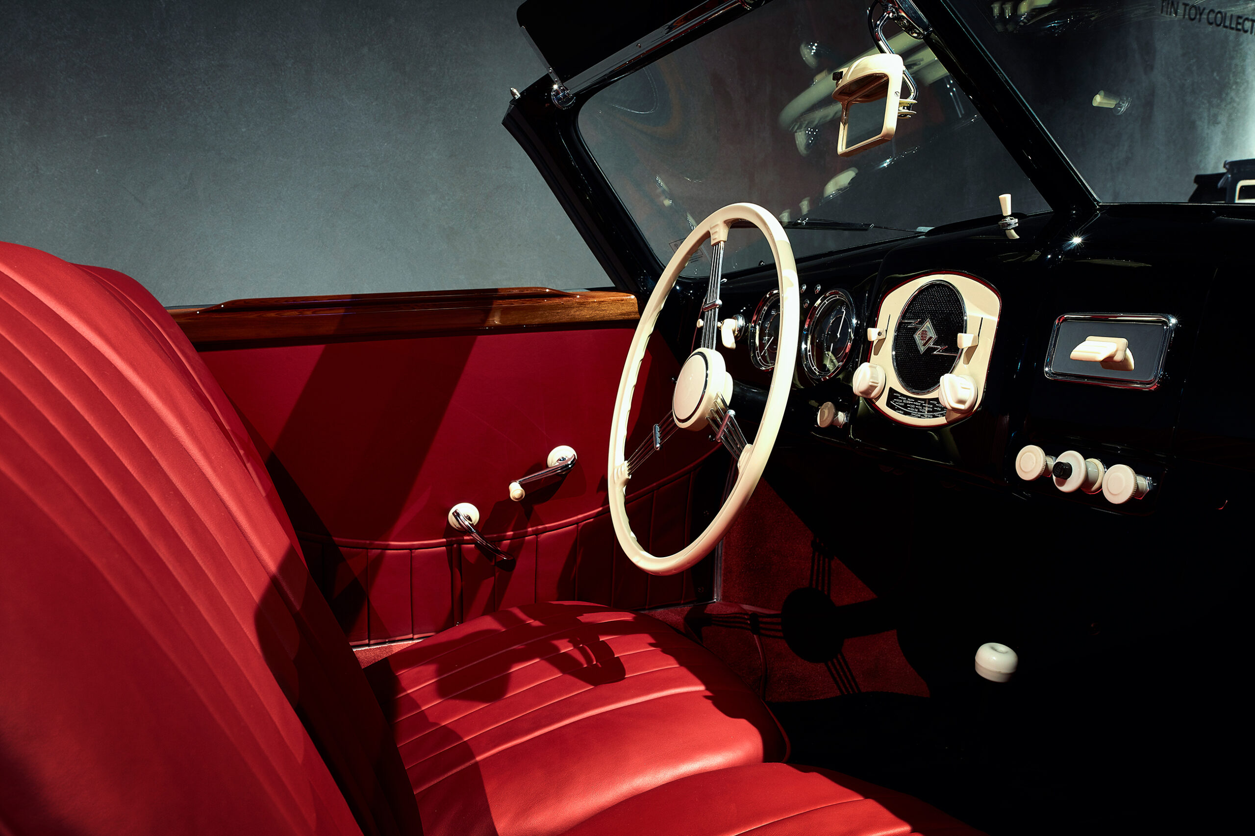 Innenraum eines klassischen Oldtimers mit roten Ledersitzen, weißem Lenkrad und Armaturenbrett-Bedienelementen und Zifferblättern im Retro-Stil, wobei das Sonnenlicht Schatten auf die Sitze wirft.