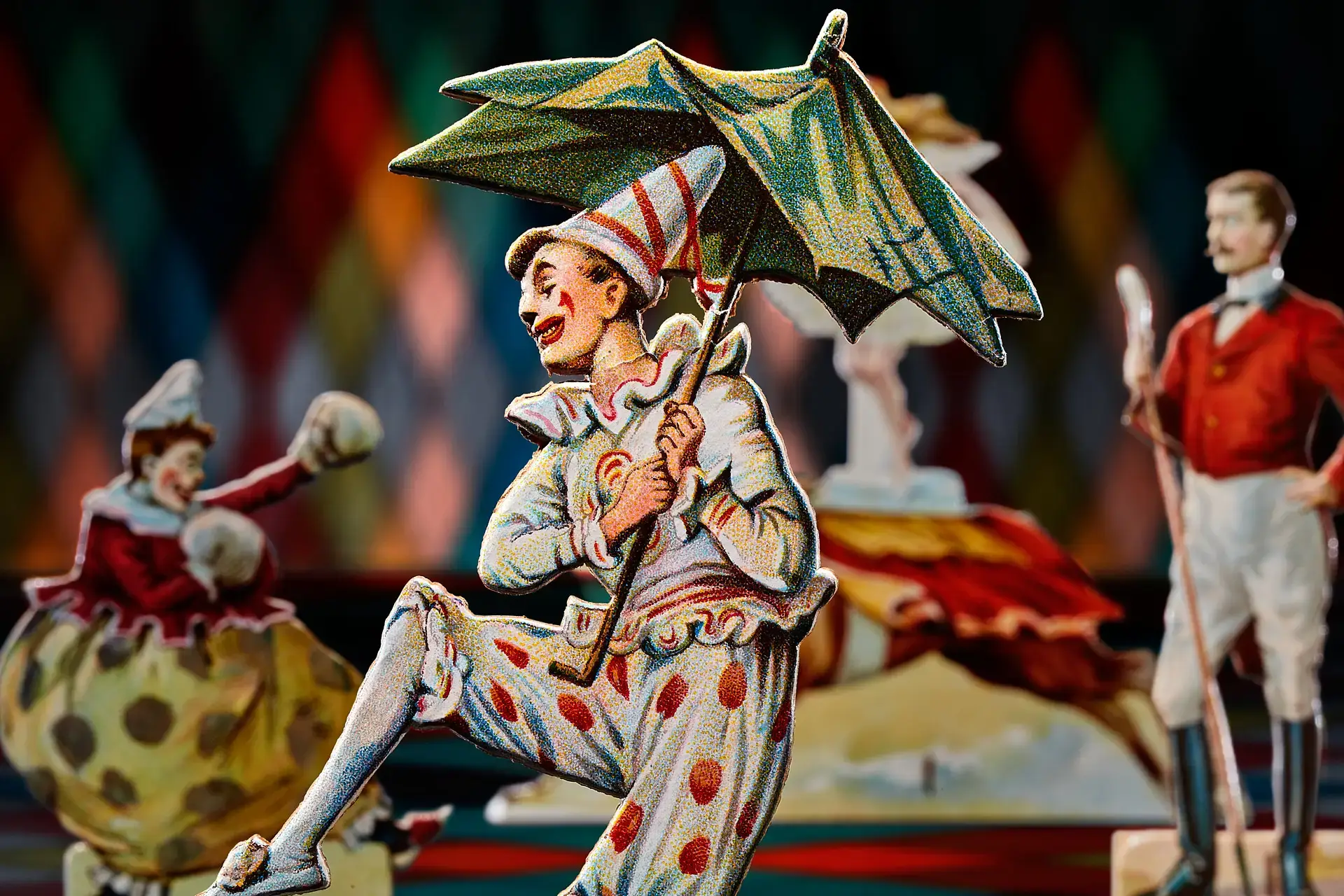 Eine Scherenschnittfigur eines Clowns im Vintage-Stil mit gepunktetem Kostüm und Hut hält lächelnd einen grünen Regenschirm, während andere skurrile Zirkusfiguren in bunter Kleidung im Hintergrund des Traumwerks, einem beliebten Ausflugsziel, verschwimmen.