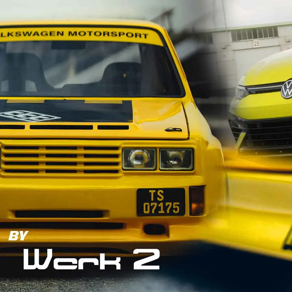 Ein gelber Volkswagen Rennwagen mit Volkswagen Motorsport auf der Windschutzscheibe und einem schwarzen Nummernschild steht neben einem modernen gelben Volkswagen. Der Text BY Werk 2 erscheint am unteren Rand des Bildes.