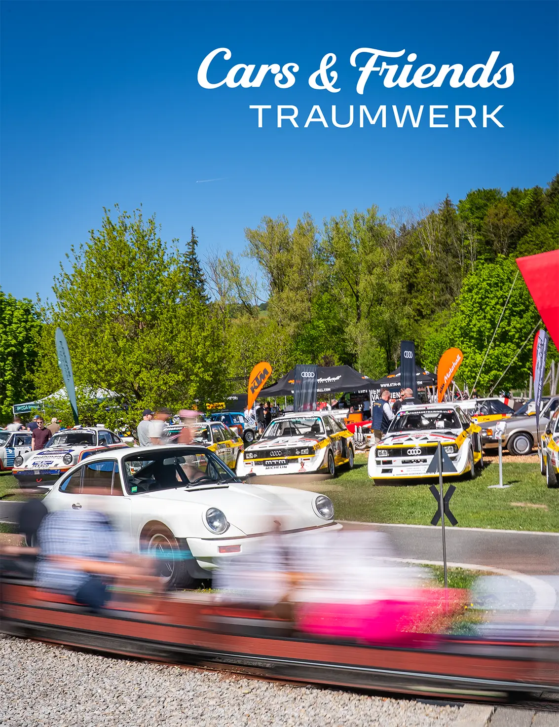Auf einer lebhaften Autoausstellung unter freiem Himmel sind klassische weiße Sportwagen und Rallye-Fahrzeuge zu sehen, um die sich eine Menschenmenge drängt. Im Hintergrund sind Bäume und Zelte zu erkennen. Oben ist der Schriftzug „Cars & Friends TRAUMWERK“ zu sehen.