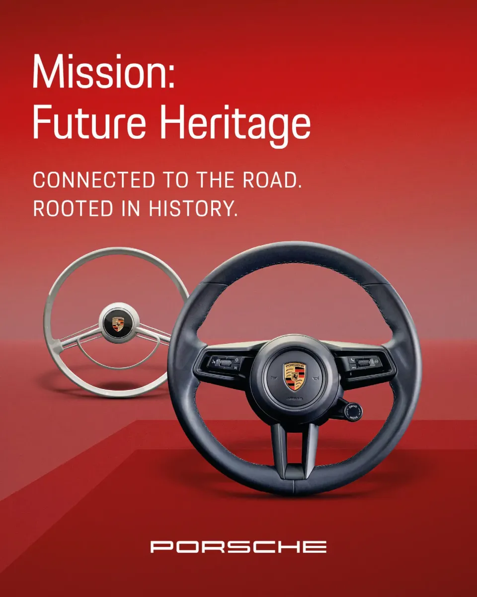 Auf rotem Hintergrund sind zwei Porsche-Lenkräder zu sehen, ein klassisches und ein modernes, mit dem Text: Mission: Future Heritage. Verbunden mit der Straße. Verwurzelt in der Geschichte. Das Porsche-Logo befindet sich am unteren Rand.