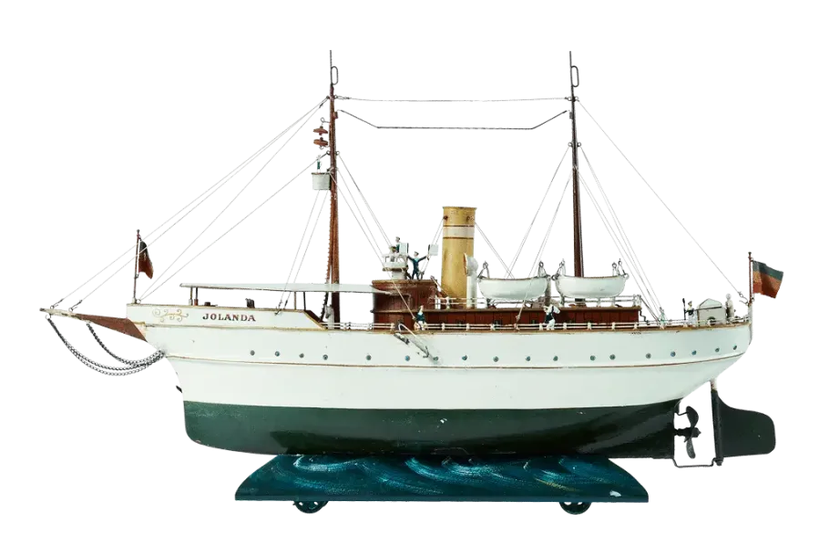 Schiffsmodell namens Jolanda mit weißem Rumpf, braunem Deck, zwei Rettungsbooten und detaillierten Masten mit Takelage; ausgestellt auf einem blauen wellenförmigen Ständer vor weißem Hintergrund.